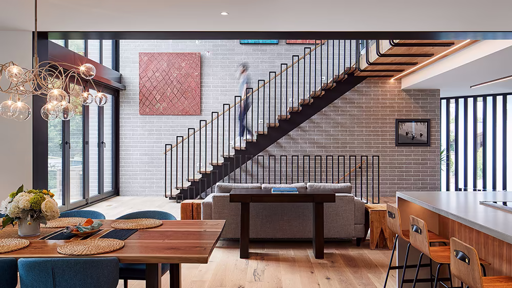 Photograph of the finished interior showing the main living area and staircase with warm wood floors and modern furnishings.